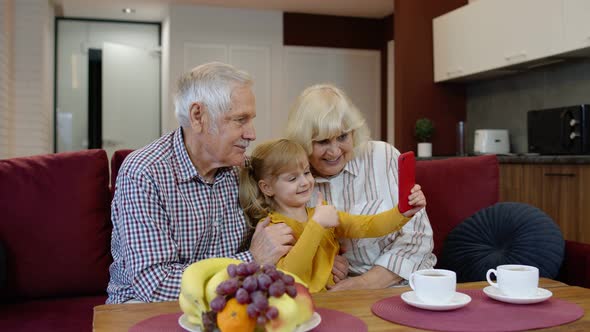 Senior Caucasian Couple with Cute Child Girl Granddaughter Using Mobile Phone, Watching Funny Videos