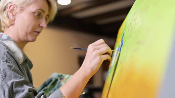 Happy Woman Paints on Canvas Using Thin Brush