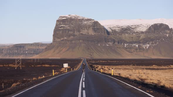 Man Jumps on an Empty Asphalt Road in Front of Majestic Mountains in Iceland