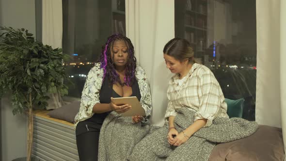 Female Friends in Bedroom looking at digital tablet. An African American woman Uses a Tablet