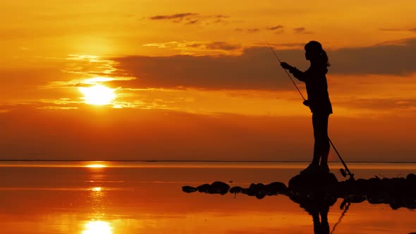 Woman Fishing on Fishing Rod Spinning at Sunset Background