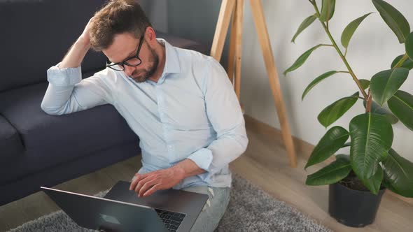 Man with Glasses Sitting on Carpet with Laptop and Working in Cozy Room