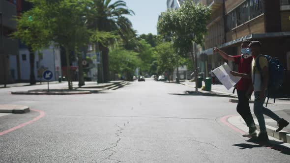 Two mixed race male friends wearing face masks, walking, using map in the street