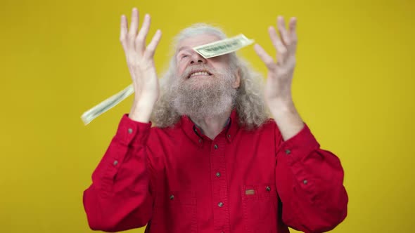 Excited Happy Senior Man Standing at Yellow Background As Dollars Falling in Slow Motion