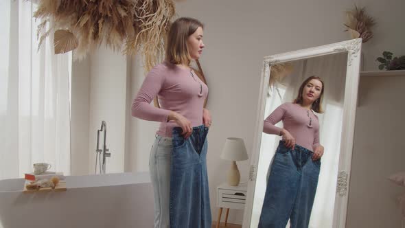 Proud Positive Slim Woman Showing Old Oversized Jeans After Weight Loss Indoors