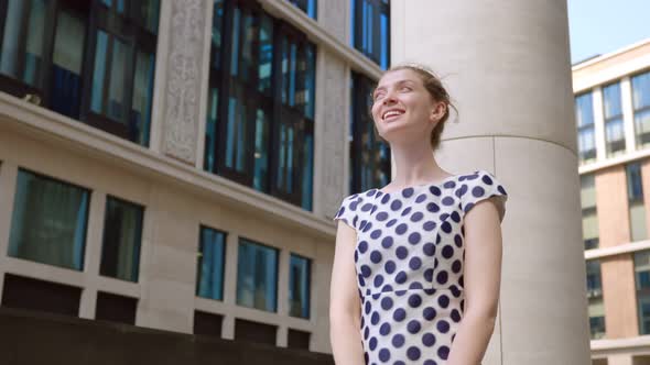 Arc Shot of Young Smiling Woman Looking Up at Modern Business Center Standing Outdoors