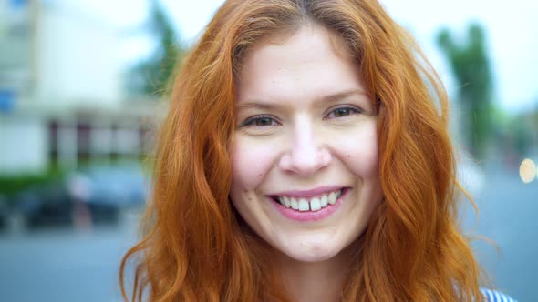 Red-haired Girl portrait. Beautiful Redhead Young Woman Smiling Looking at Camera Outdoors