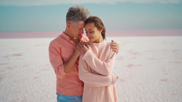Affectionate Man Gently Embracing Young Attractive Woman in Pink Sweater on White Salty Coast of