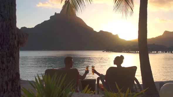 Man and woman couple toasting, drinking drinks, tropical island resort, lagoon and Mount Otemanu