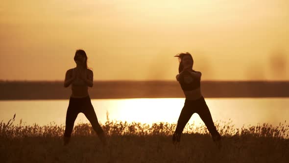 Silhouettes of Two Beautiful Girls Dancing Zumba in Field at Sunrise