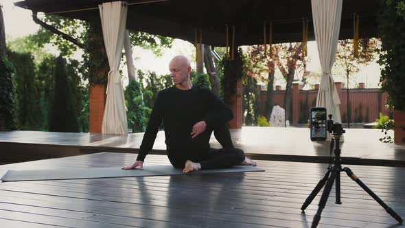 Sportsman in Black Sportswear Suit is Practicing Yoga Sitting on Mat and Wooden Floor of Veranda