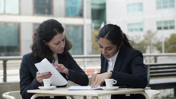 Focused Businesswomen with Papers in Cafe