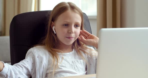 Blonde Teenage Girl Wears Headphones, Sits Ate Home Table, Looks at Laptop, Communicates on Video