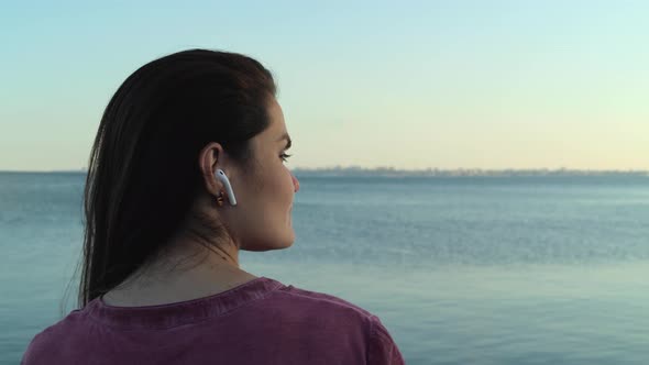 A Young Woman Listens To Music By The Sea And Looks At A Distant City