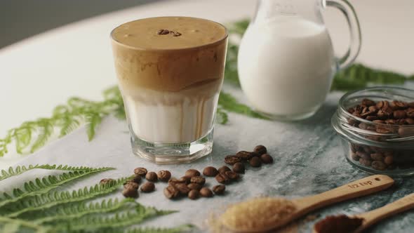 Dalgona coffee with almond milk and brown sugar, coffee beans and green plant on marble board.