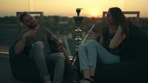 Young Attractive Couple. The Guy with the Girl Smoke Hookah at Sunset and Laugh