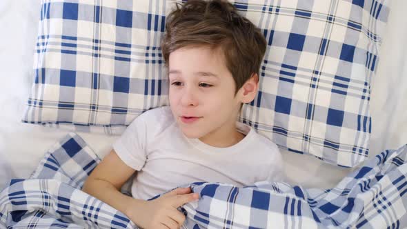 Happy Preschooler Boy Enjoying Comfortable Bedding in Bed Smiling at Camera