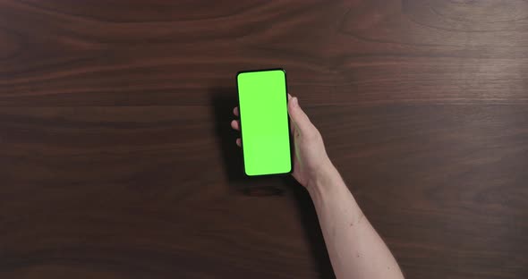 Top View Man Hand Using Smartphone with Green Screen Over Black Walnut Wood Table