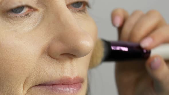 Make Up Artist Do Makeup with Highlighter Concealer to Middleaged Woman with Blue Eyes