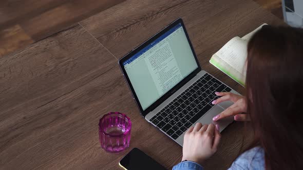 Woman Typing on a Laptop Keyboard While Sitting at a Table with a Glass of Water