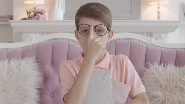 Serious Caucasian Boy Adjusting Eyeglasses and Looking at Camera. Portrait of Charming Smart Child