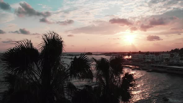 Sunset in tourist city Paphos with palm trees and stormy sea with waves hitting beachfront splashing