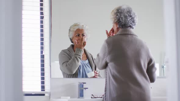 African american senior woman applying face cream while looking in the mirror at home