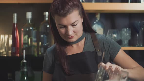 Attractive bartender pouring mixed drink in speakeasy bar, dolly shot.