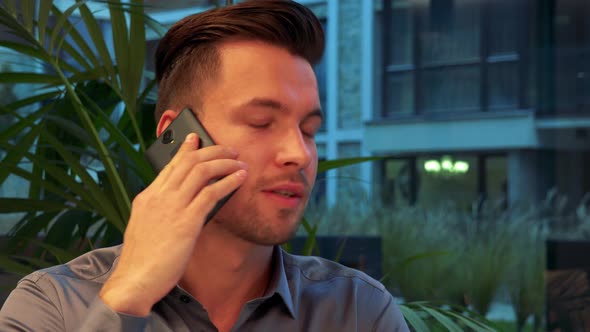 A Young, Handsome Man Sits at a Table in a Restaurant and Talks on a Smartphone