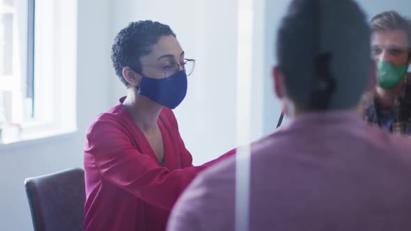 Diverse colleagues wearing face masks discussing together in meeting room at modern office