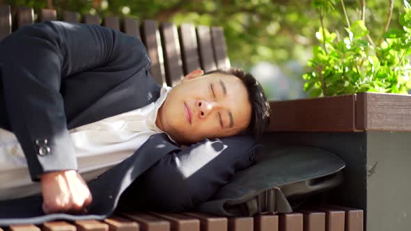 exhausted and overworked young asian businessman lying on a bench in the city central park outdoors.
