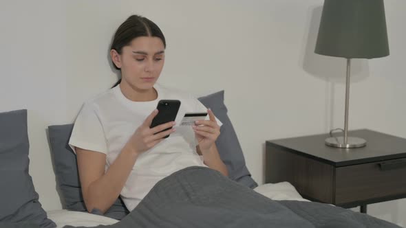 Hispanic Woman Making Online Payment on Smartphone in Bed