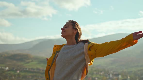 Young Woman Wearing a Yellow Jacket Raising Her Arms Into the Blue Sky and Enjoying the View Above