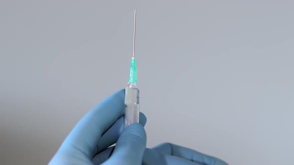 Extreme close up shot of doctor's hands wearing surgical gloves and squirting air from syringe throu