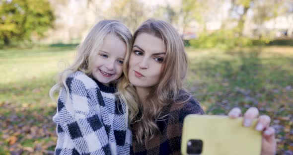 Happy mother and daughter taking a selfie or having a video call at park