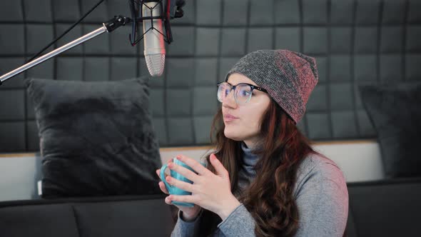 Woman drinks hot tea or coffee from cup at cozy sound recording studio in the morning