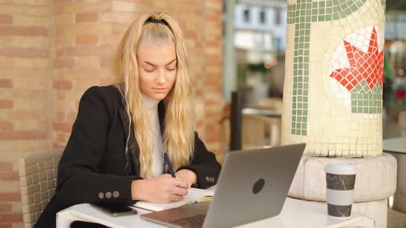 Freelancer woman writing notes while working with laptop in cafe