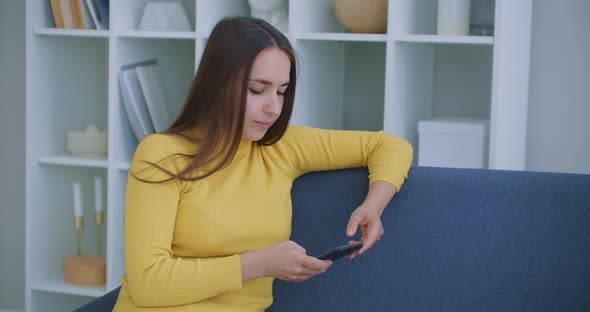 Woman Writes Messages Using Mobile Phone Sitting on Sofa in Living Room