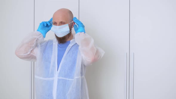 A Bald Bearded Man in a Locker Room Puts on Gloves a Mask and Glasses Before Visiting an Infected