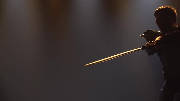 Men Fight with Swords in a Dark Studio with Stage Lighting. Silhouettes of Male Actors in Armor