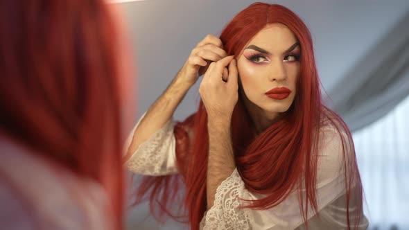 Confident Genderfluid Caucasian LGBT Woman in Red Wig Admiring Reflection in Mirror