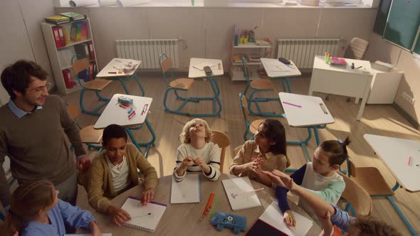 Smiling Schoolteacher Explaining Lesson to Students at Round Table