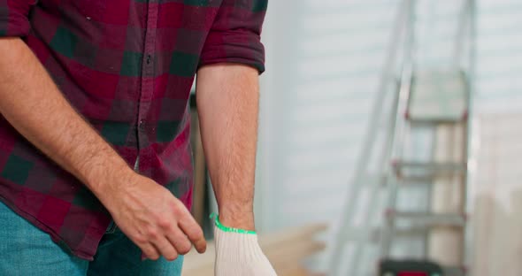 A Young Carpenter Wearing Jeans and a Plaid Flannel Shirt Puts on White Cloth Protective Gloves