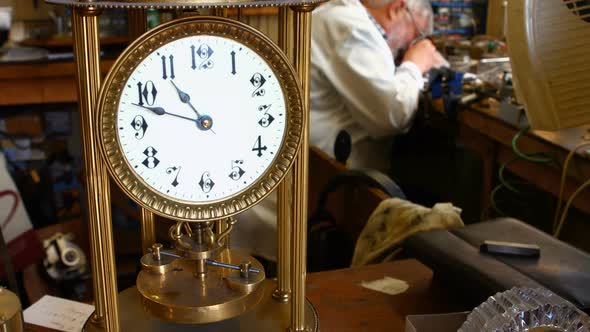 Vintage torsion pendulum clock on table while horologist working in background