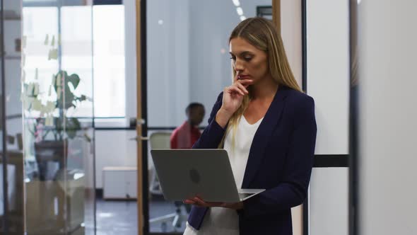 Smiling caucasian woman using laptop while standing at modern office