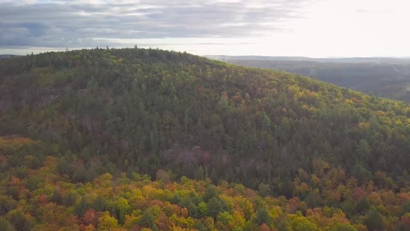Aerial Daytime Wide Shot Flying Over Fall Forest Colors Orbiting A Huge Tall Rocky Cliff Ridge And M