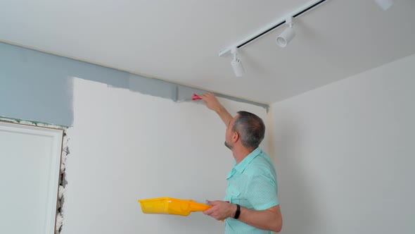 A Man in a Shirt Paints the Walls with a Roller Gray