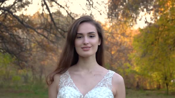 Young Brunette Woman in Long White Dress Walks Along Autumn Colorful Forest at Sunset