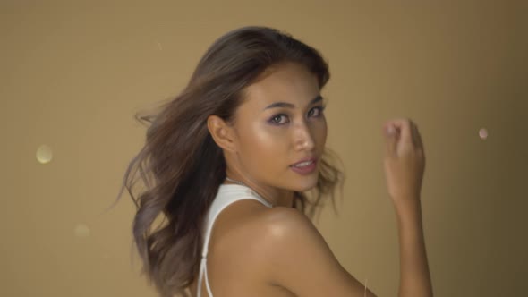 Stunning Asian model poses with the wind in her hair and glitter bokeh in the blowing air and beige