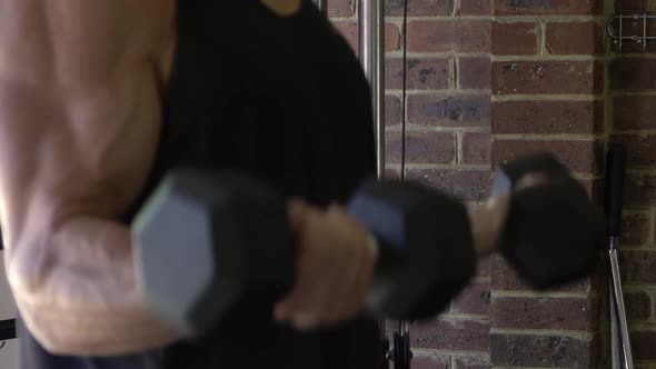 Muscly man in home gym exercising dumbbell bicep curls blurry bokeh shot